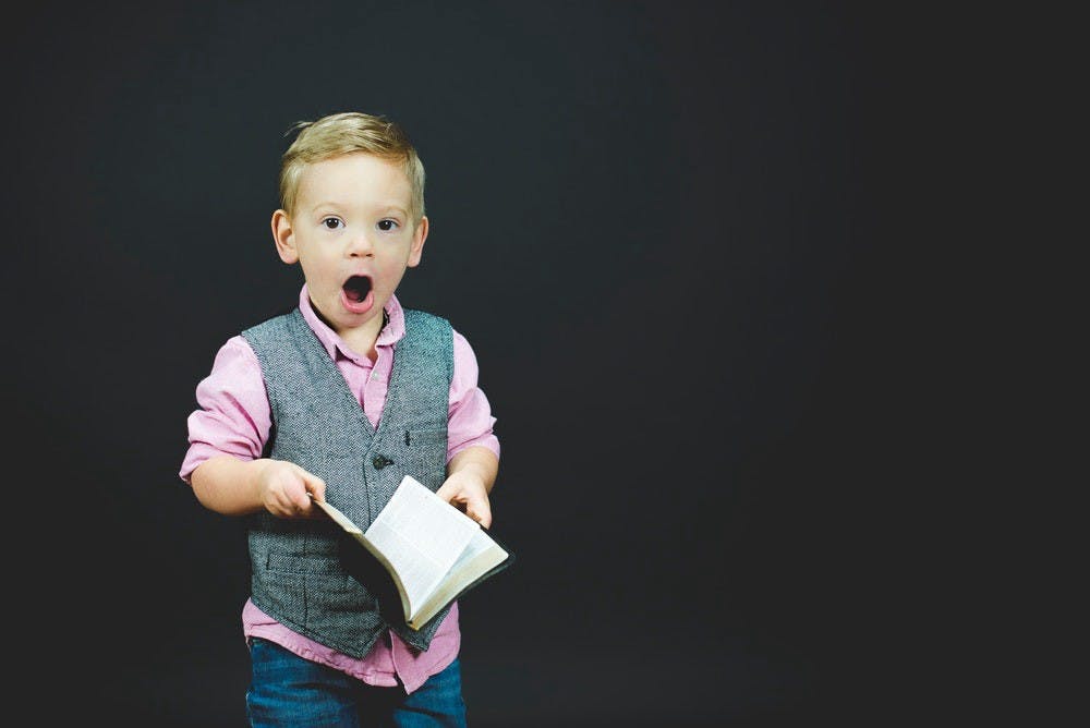 A child holding a book, with a shocked face.