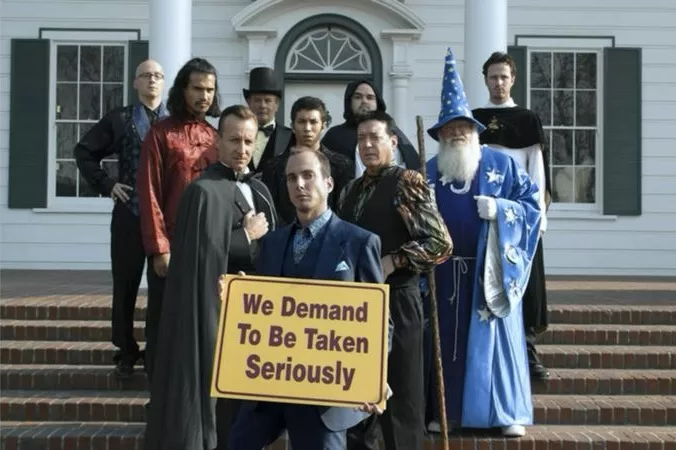 A collection of people dressed in wizard garb, holding a sign saying 'We demand to be taken seriously.' Image from Arrested Development.